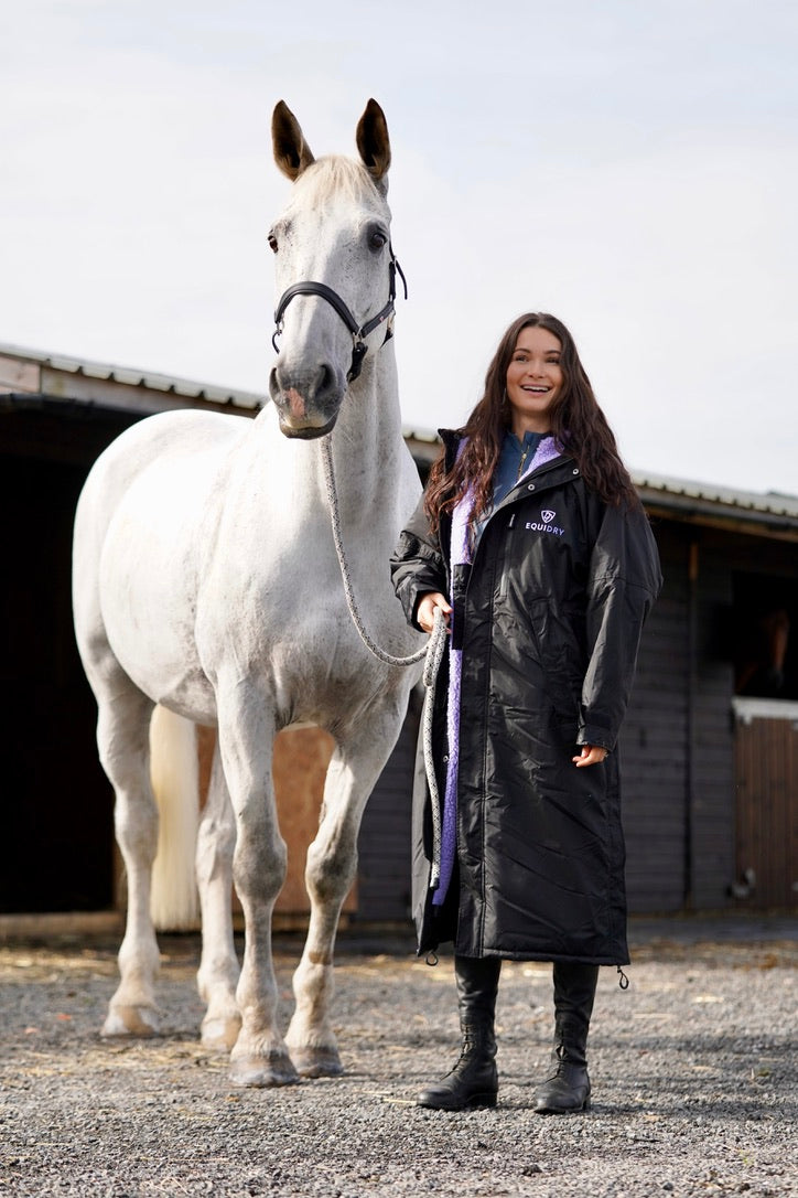 EQUIDRY women's long waterproof horse riding coat in Black/Lilac rider holding horse on yard