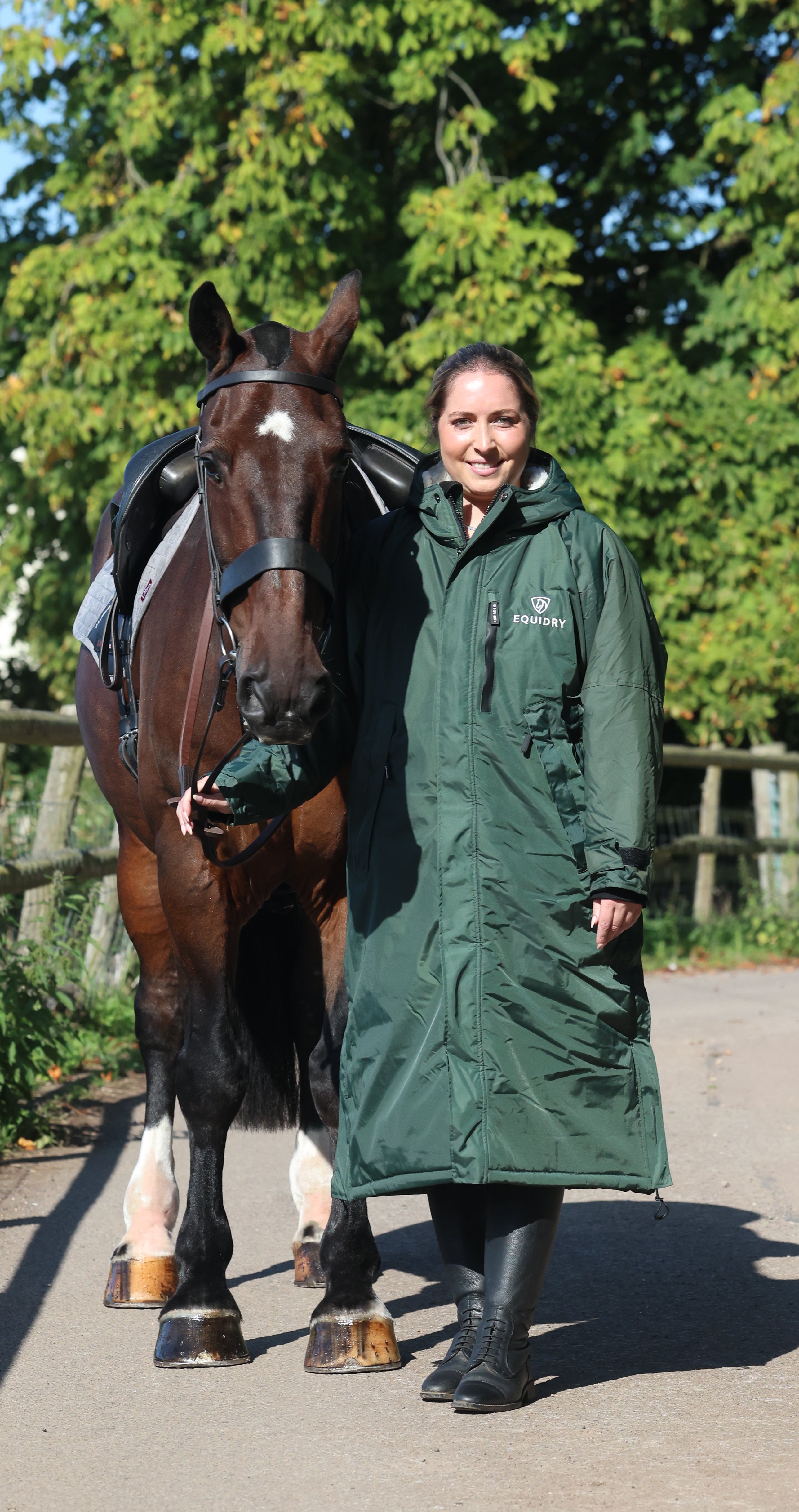 Equidry waterproof horse riding coat. Woman in long green jacket with horse. Equestrian apparel for women
