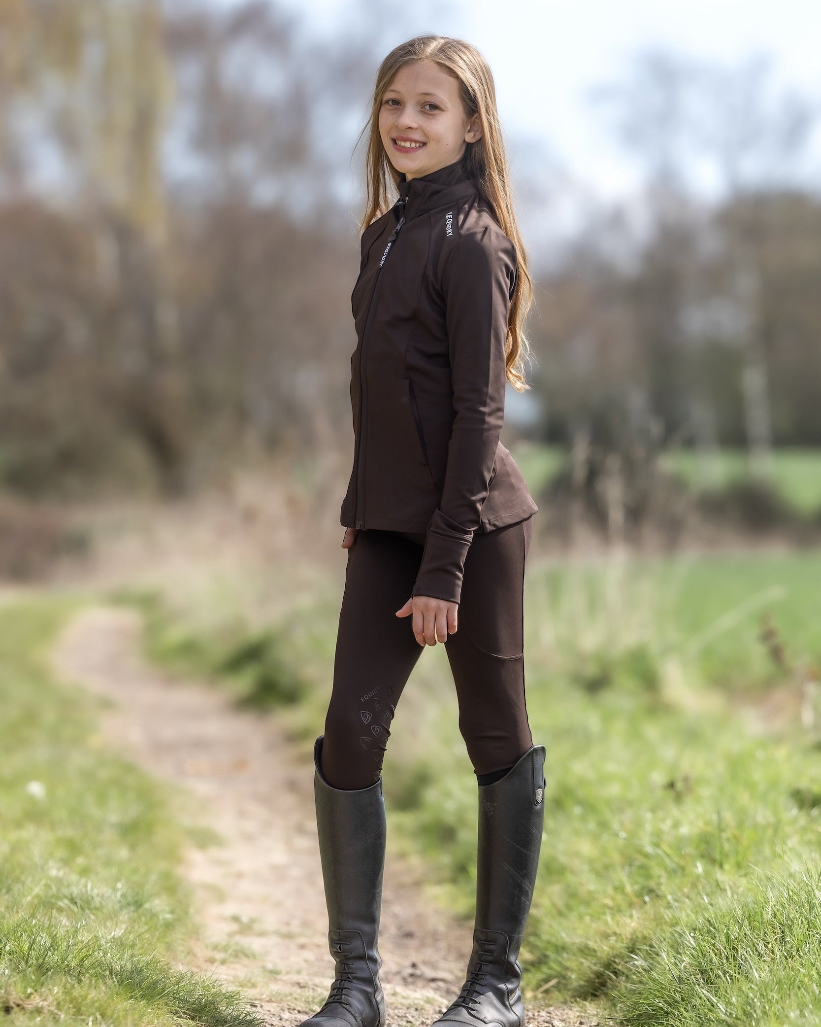 Child in EQUIDRY Brown Zip Up Top & Leggings. Riding Apparel by Equiflair. Long brown hair, outdoors, equestrian fashion. Water repellent.