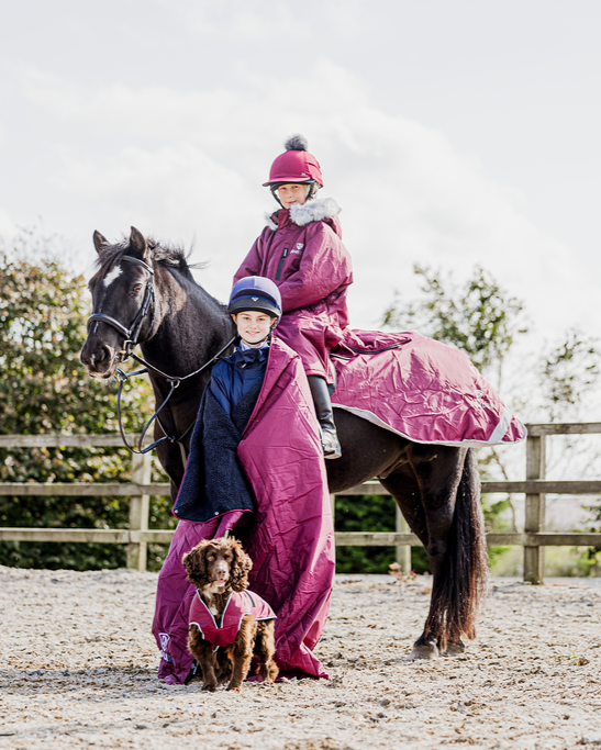 EQUIDRY Evolution Lux children's Warm Waterproof Winter Horse Riding Coat Thick Fleece Lining with Faux Fur Trim Hood being shown in plum with horse and dog