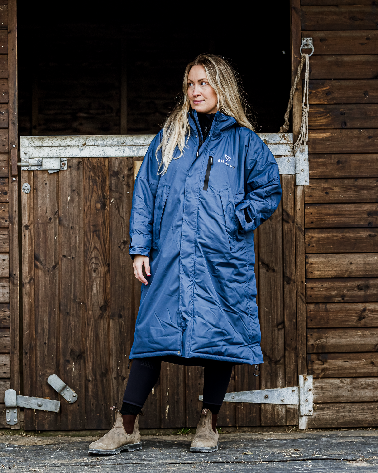 Woman in EQUIDRY Evolution Steel Blue Riding Coat outside stable: Equestrian waterproof fleece lined coat for women.