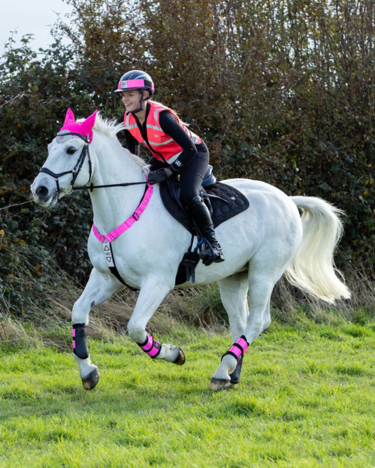 WOOF WEAR Hi Vis Pink Riding Vest: Rider on horse wearing fluorescent visibility vest for equestrian safety.