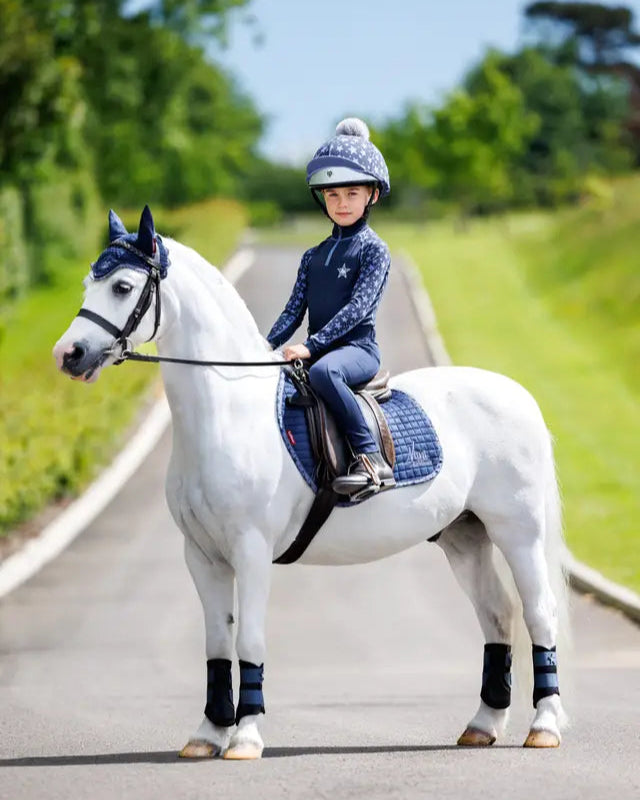 Child equestrian in LEMIEUX MINI BASE LAYER INDIGO riding white pony. Equiflair riding outfit.
