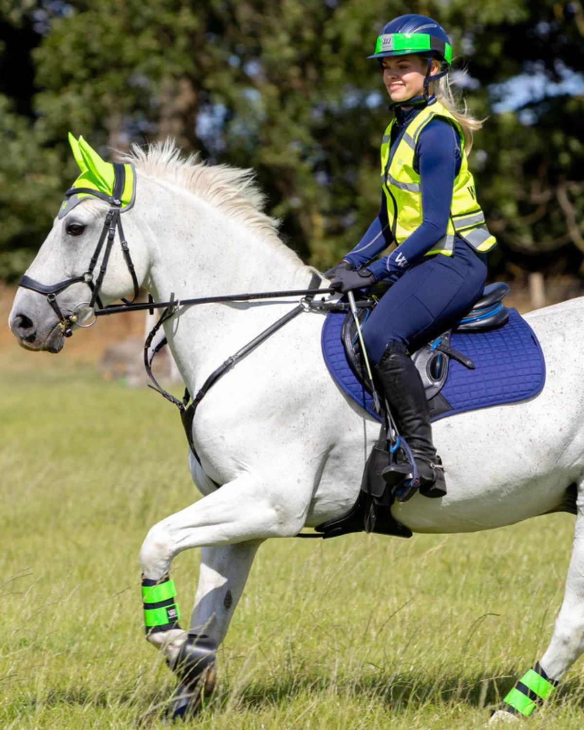 Horse rider in Woof Wear hi viz riding vest for equestrian safety. White horse with green accents.