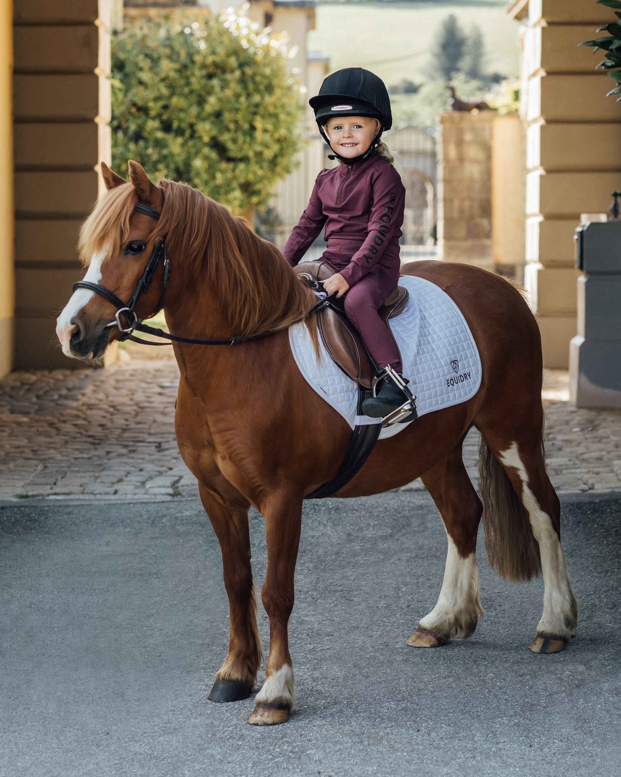 Young equestrian rider on pony wearing EQUIDRY plum/black base layer. Children's horse riding apparel from Equiflair.