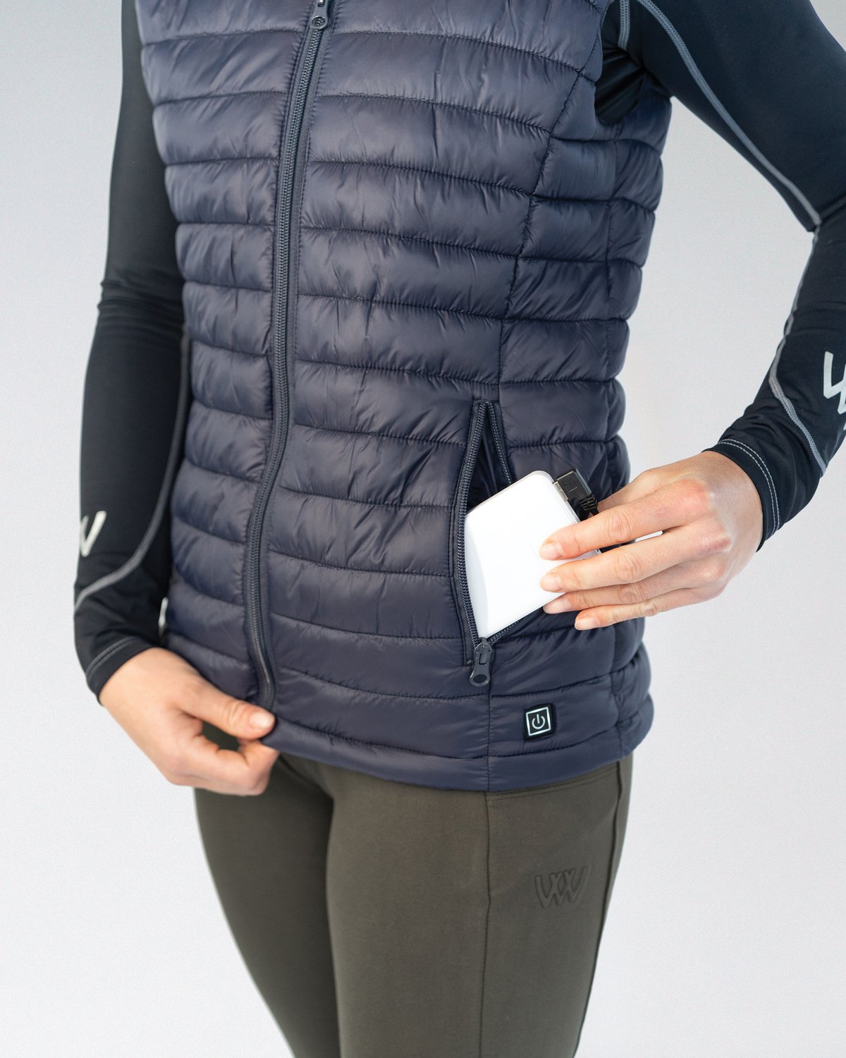 Woof Wear Heated Gilet Navy: Woman Inserting Power Bank. Battery Operated Vest, Core Warming. Powerbank Sold Separately