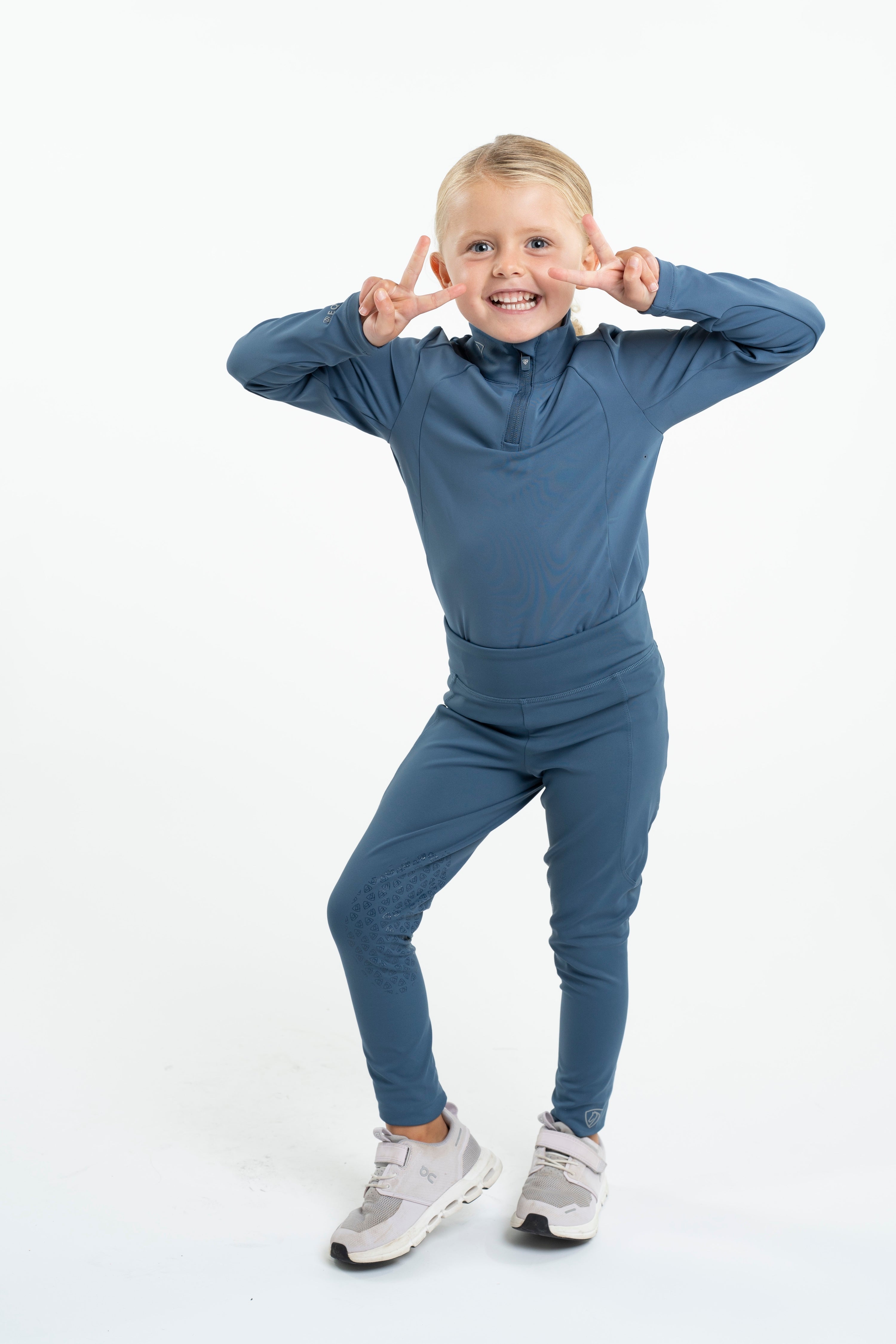 Girl in EQUIDRY Kids Riding Leggings: Steel Blue Equestrian Apparel with Knee Grips, Water Repellent, and Comfortable Design