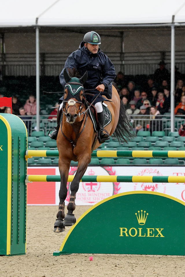 Horse and rider jumping a Rolex obstacle in show jumping event. Rider wearing a navy Equidry jacket. Equestrian…
