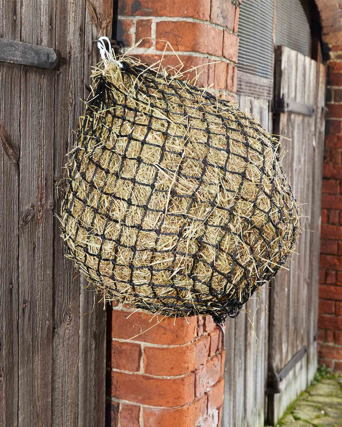 Hay Net for Horses: Black Mesh Haylage Feeder Filled with Hay Hanging on Wood and Brick | Horse Feeding Supplies