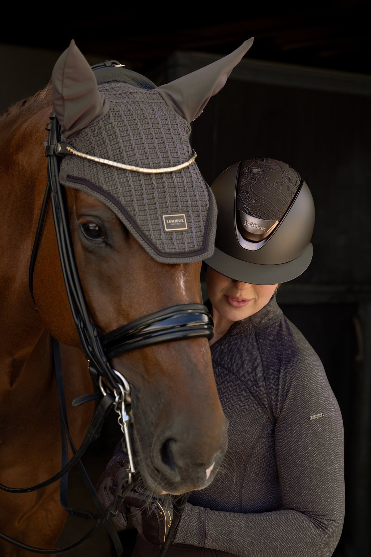 Brown horse wearing LeMieux cocoa fly hood, rider in helmet with herringbone pattern