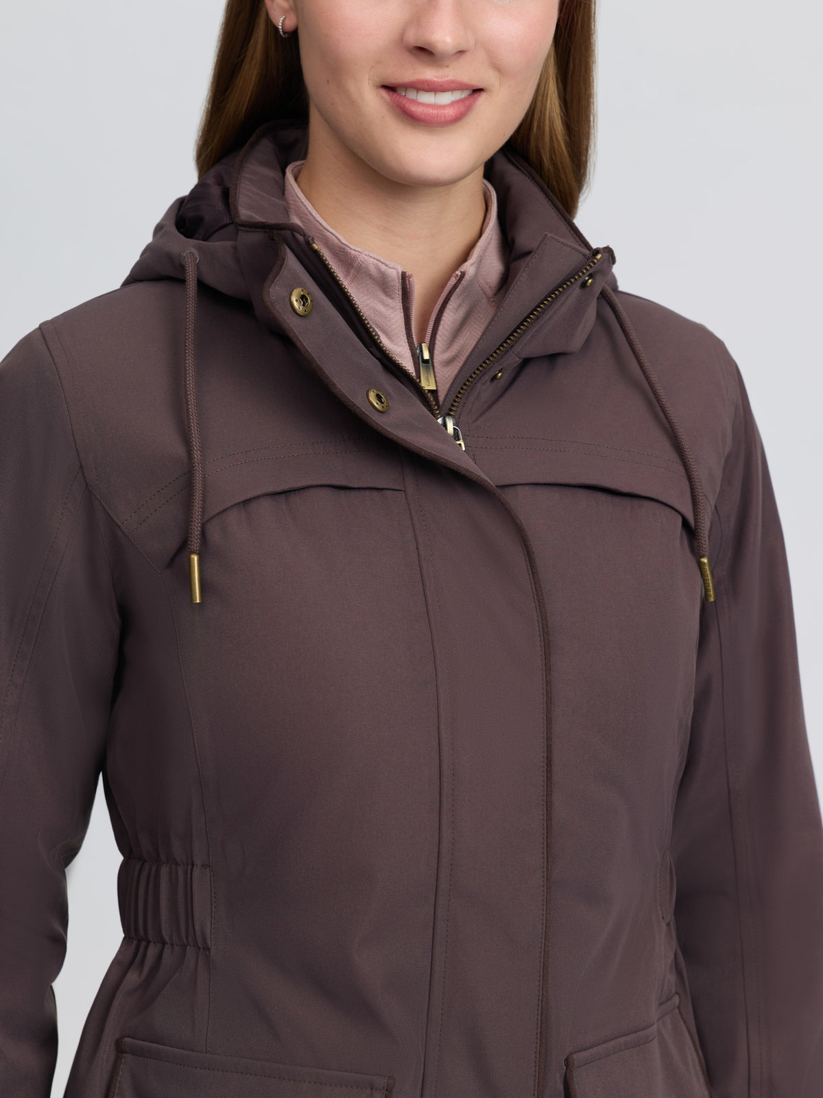 Woman wearing LeMieux Heritage Beatrice Waterproof Coat in Cocoa brown with hood and zip.