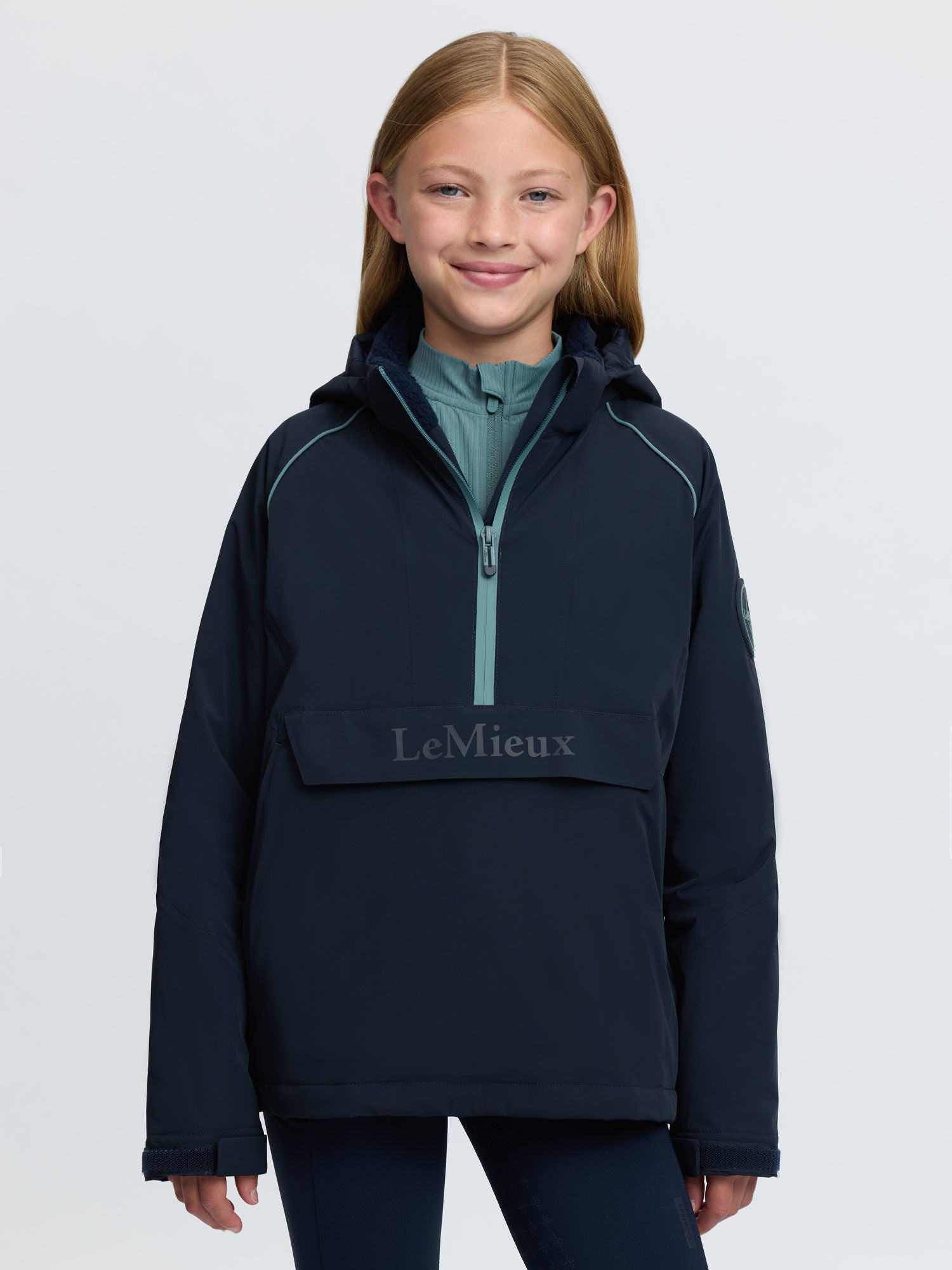 Young girl in navy LeMieux waterproof anorak with hood and half-zip.