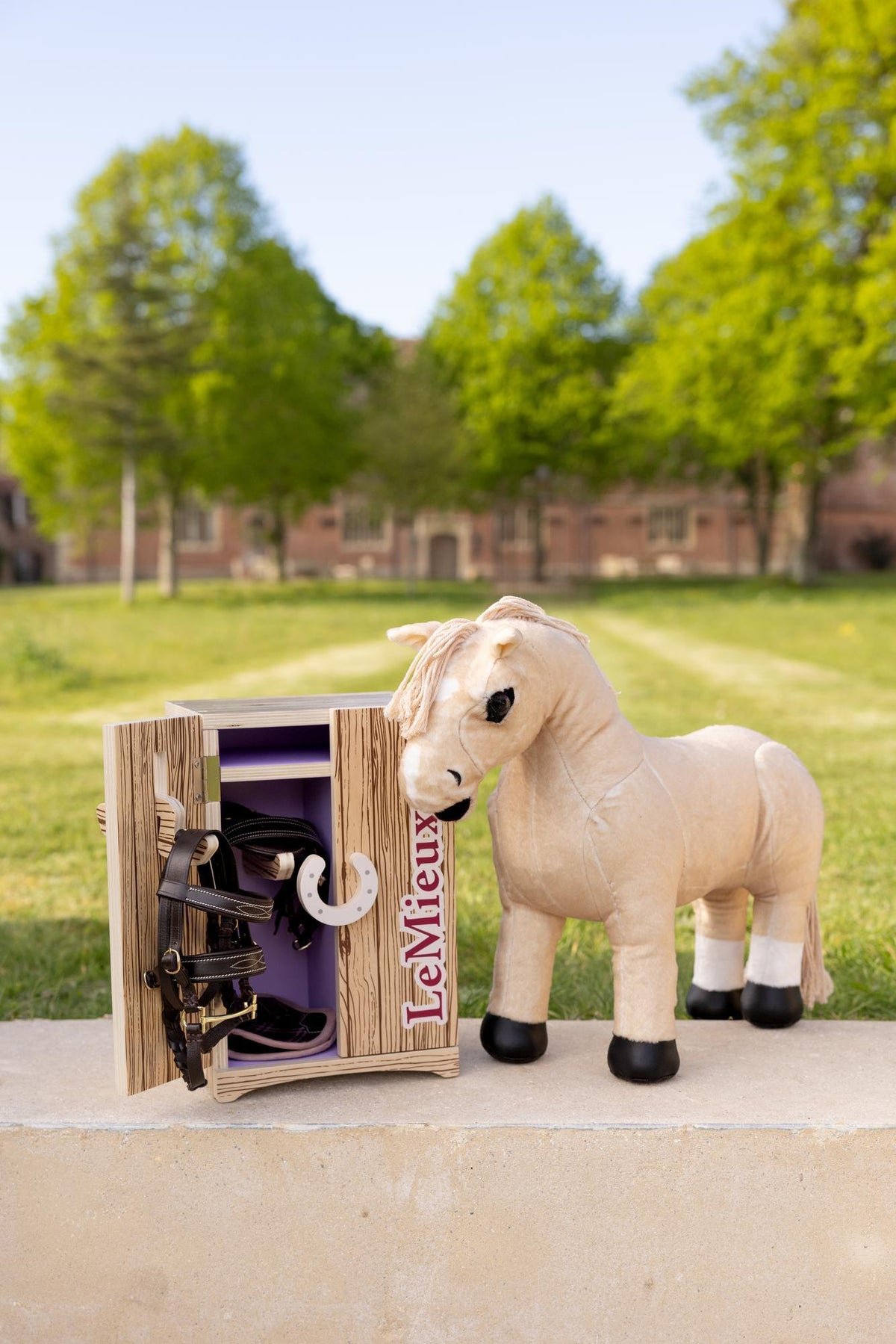 LeMieux toy pony with wooden tack locker and equestrian accessories on a grassy lawn.