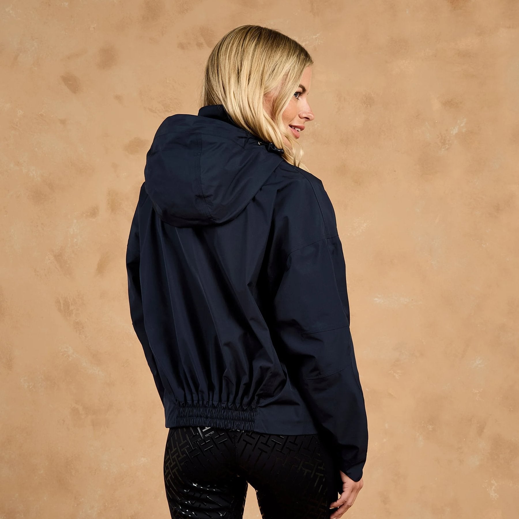 Woman in navy blue Toggi Meyer waterproof hooded blouson jacket, seen from the back and side profile.