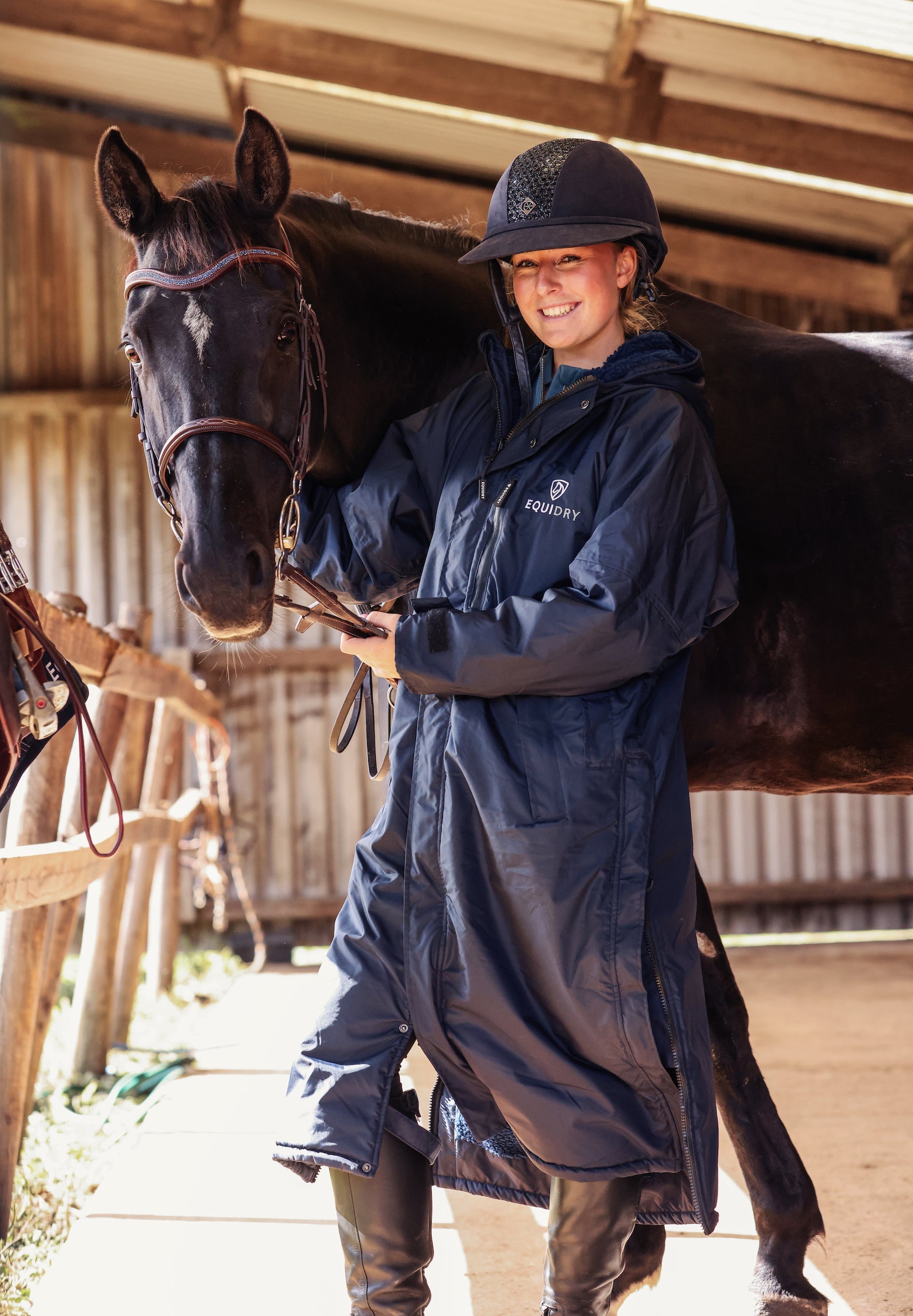 EQUIDRY women's long waterproof horse riding coat in Dark Navy/Navy modelled by rider stood on yard with horse