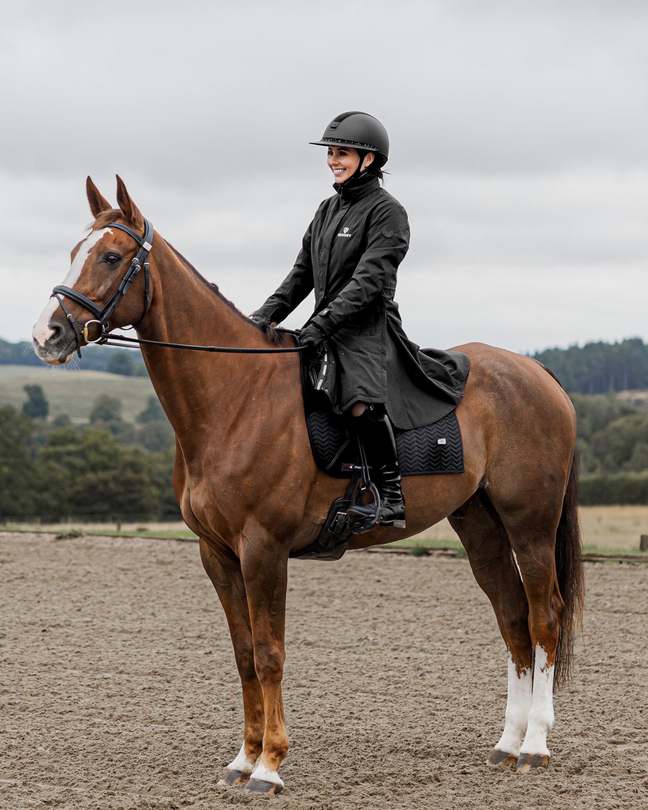 Equestrian: Woman in Equidry Bronte Riding Coat on Horse. Black waterproof riding coat, female rider, horse riding attire by Equiflair.