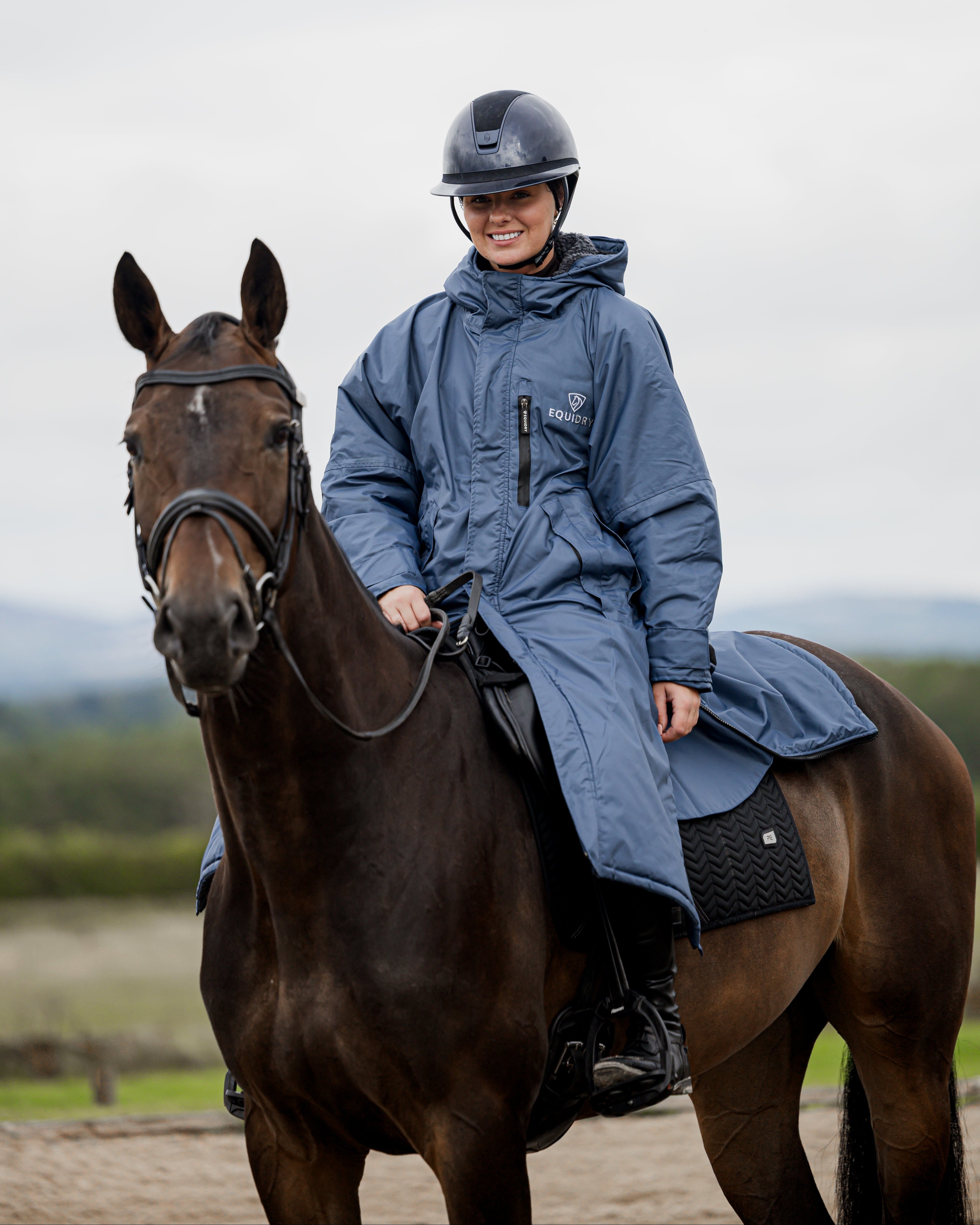 Woman horse riding in EQUIDRY Evolution steel blue waterproof fleece lined coat. Equine performance outerwear.
