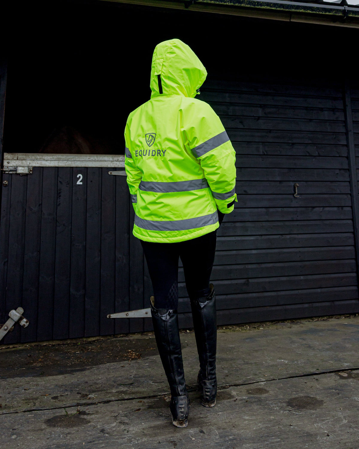 Equidry women's hi-vis yellow fleece riding coat with reflective strips, standing by a stable.