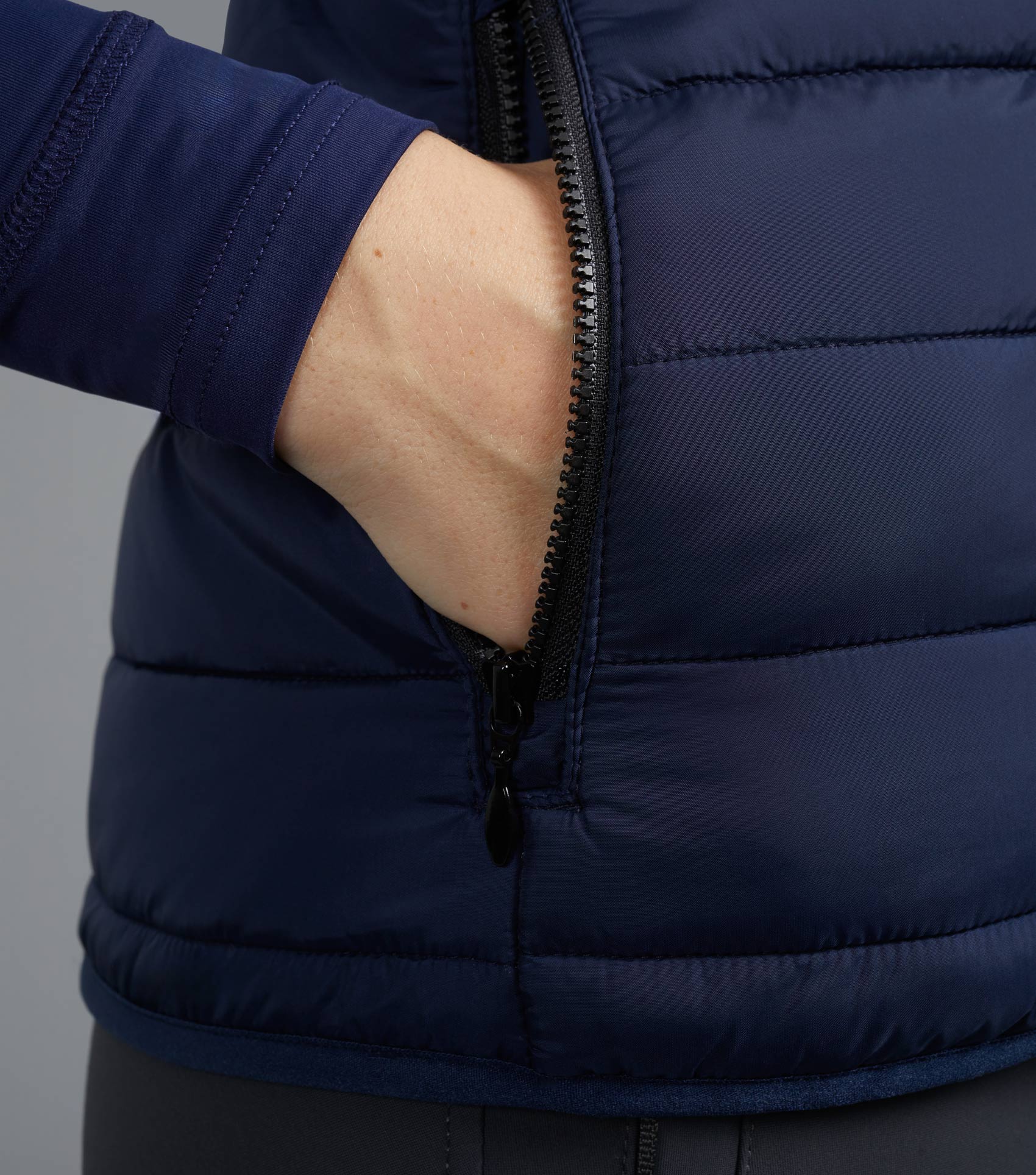 Premier Equine Navy Ladies Riding Gilet: Woman's hand in quilted equestrian vest pocket, close-up.