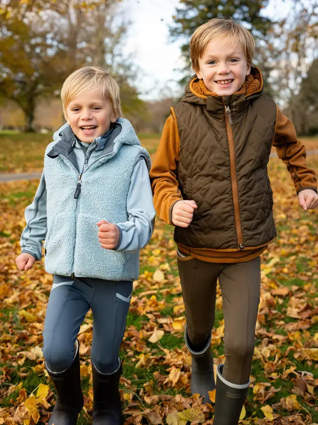 Two boys running outdoors wearing LeMieux reversible equestrian gilets, kids outdoor vests, kids equestrian clothing.