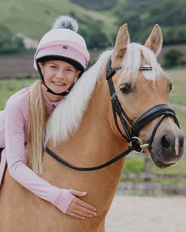 Girl in Charles Owen JS1 Pro Baby Pink horse riding helmet with horse. Equestrian gear from Equiflair. Harlow White edition.