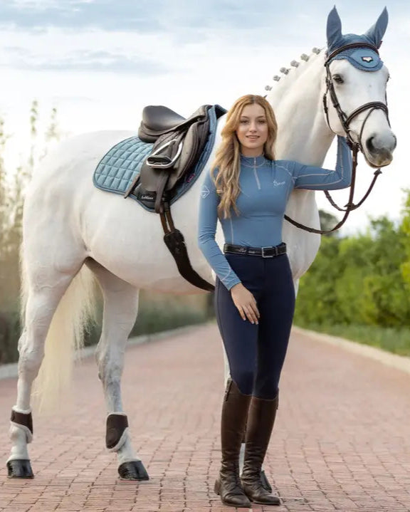 Equestrian Image: White horse with LeMieux Loire Classic Close Contact Saddle Pad in Ice Blue. Rider in blue top and riding pants.