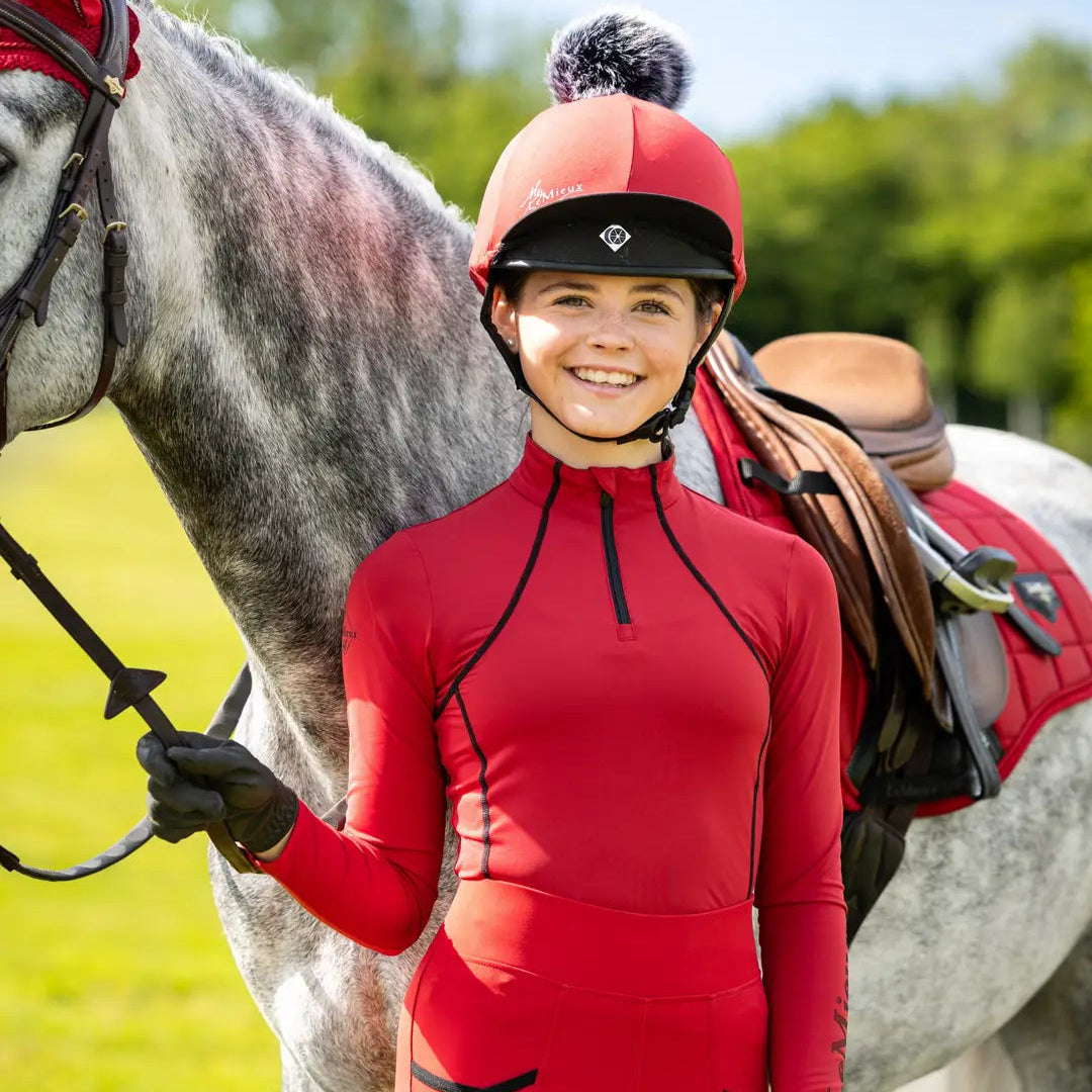 Young equestrian rider in LeMieux Chilli base layer and helmet with gray horse. LeMieux Young Rider Base Layer Chilli by Equiflair Saddlery.