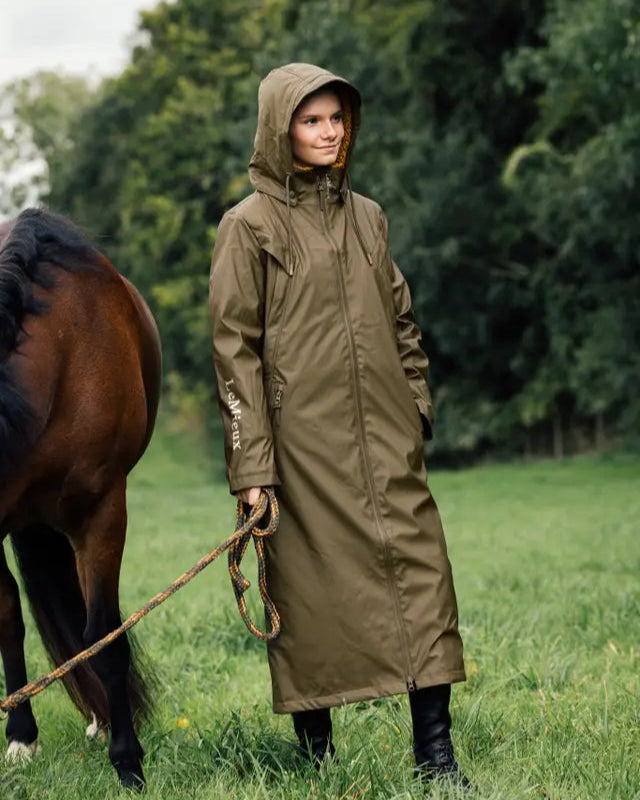 Young equestrian in Lemieux waterproof coat with hood and horse, ideal for riding in rainy weather. Equestrian apparel