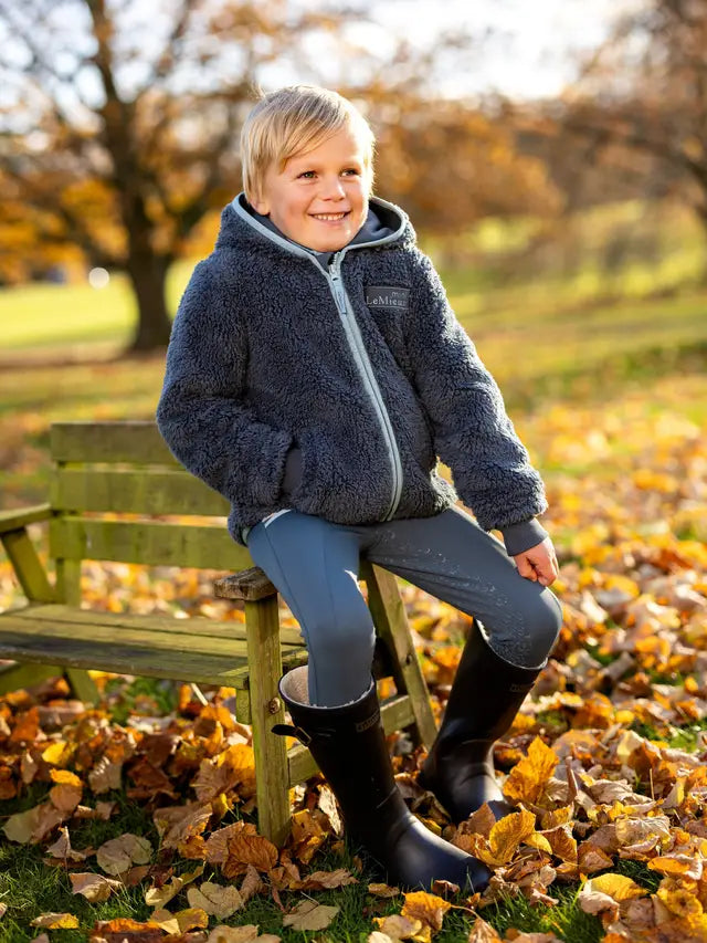 Boy in LeMieux Mini Teagan Fleece Petrol Jacket on Bench in Fall. Equestrian apparel for kids.