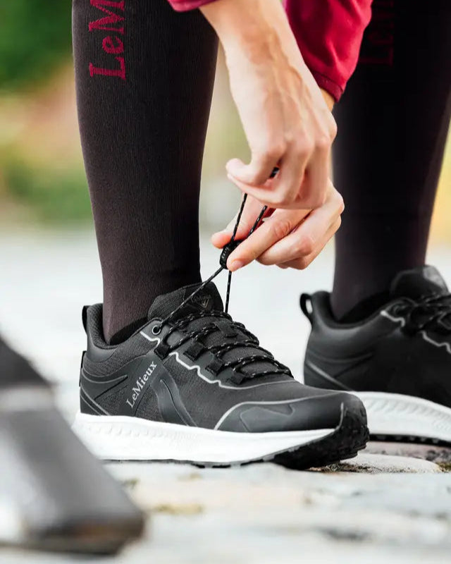 LE MIEUX TRAX 2.0 Waterproof Trainers: Black shoes being laced, perfect for equestrian activities, outdoor running & walking. Durable & comfortable
