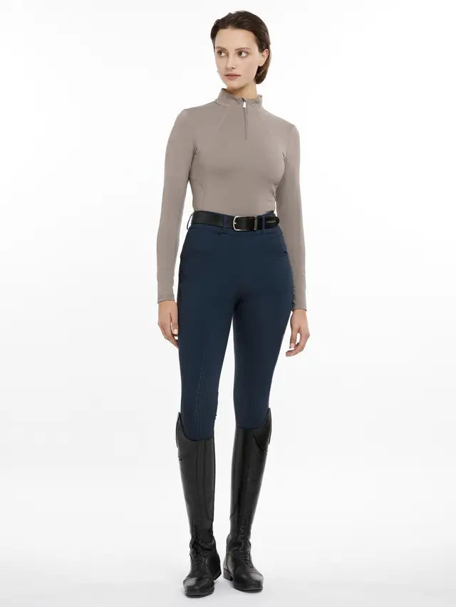 Woman wearing LeMieux Base Layer in Pecan with navy breeches and riding boots. Equestrian clothing and apparel for female riders.