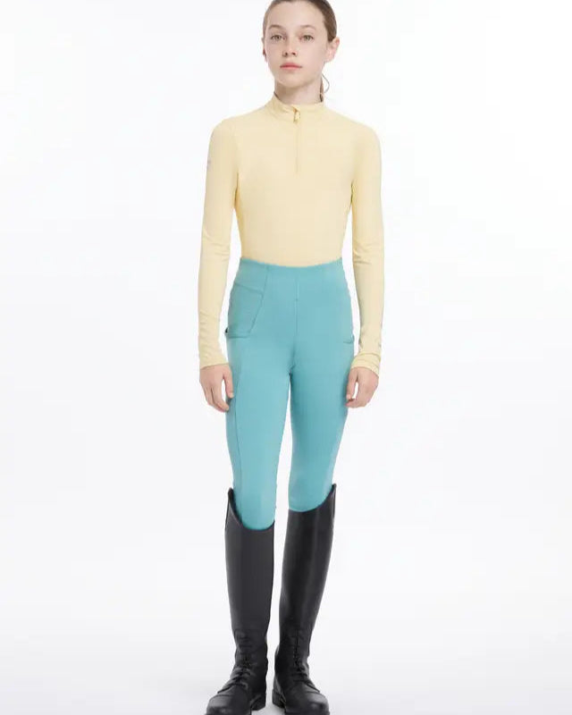Young rider in LEMIEUX Mimosa base layer and riding boots. Equestrian apparel from Equiflair.