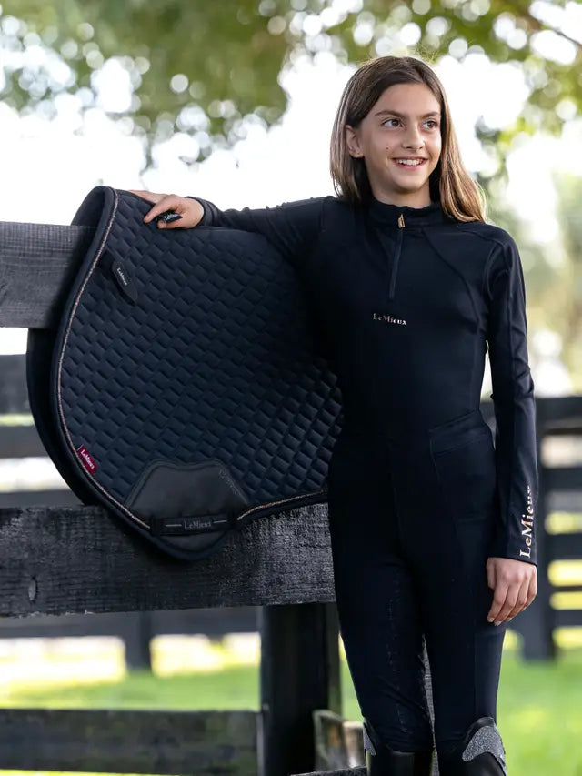 Young rider in navy LeMieux sparkle base layer and matching saddle pad by a fence.
