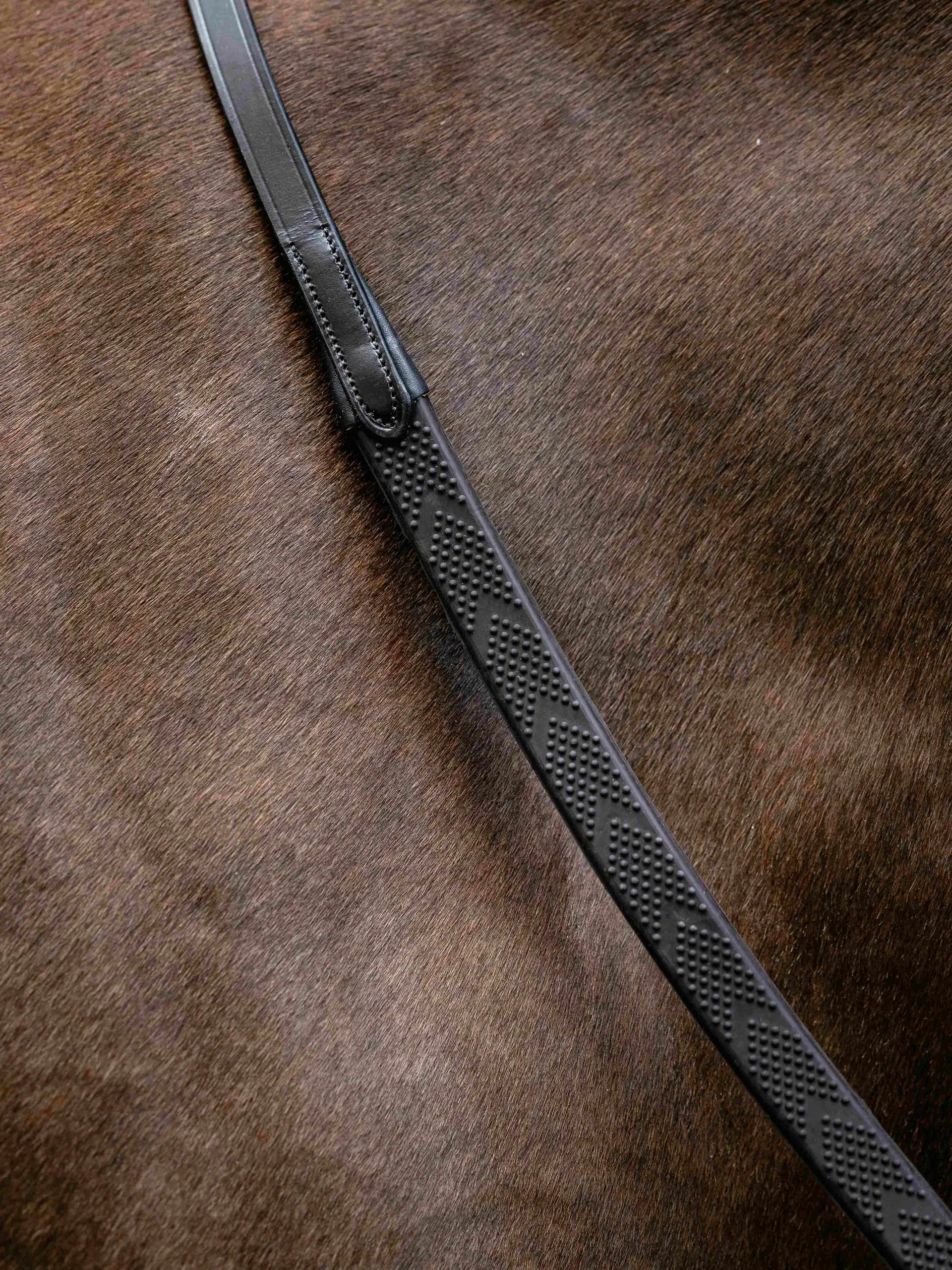 Close-up of brown horsehair with a textured black LeMieux Versa Grip rubber rein featuring dot pattern for equestrian.