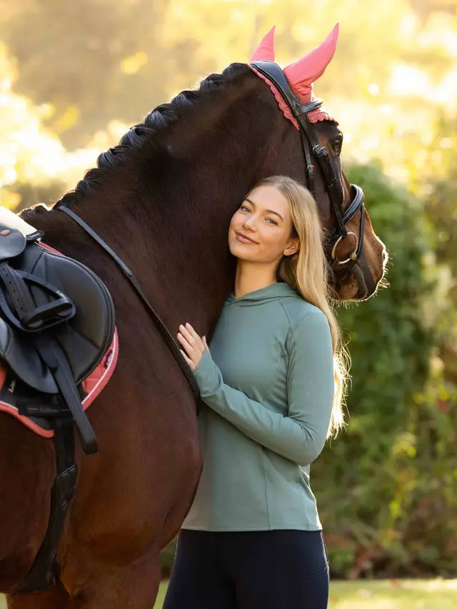 LeMieux Heidi Hooded Mid Layer Aloe equestrian training top with a woman and horse.