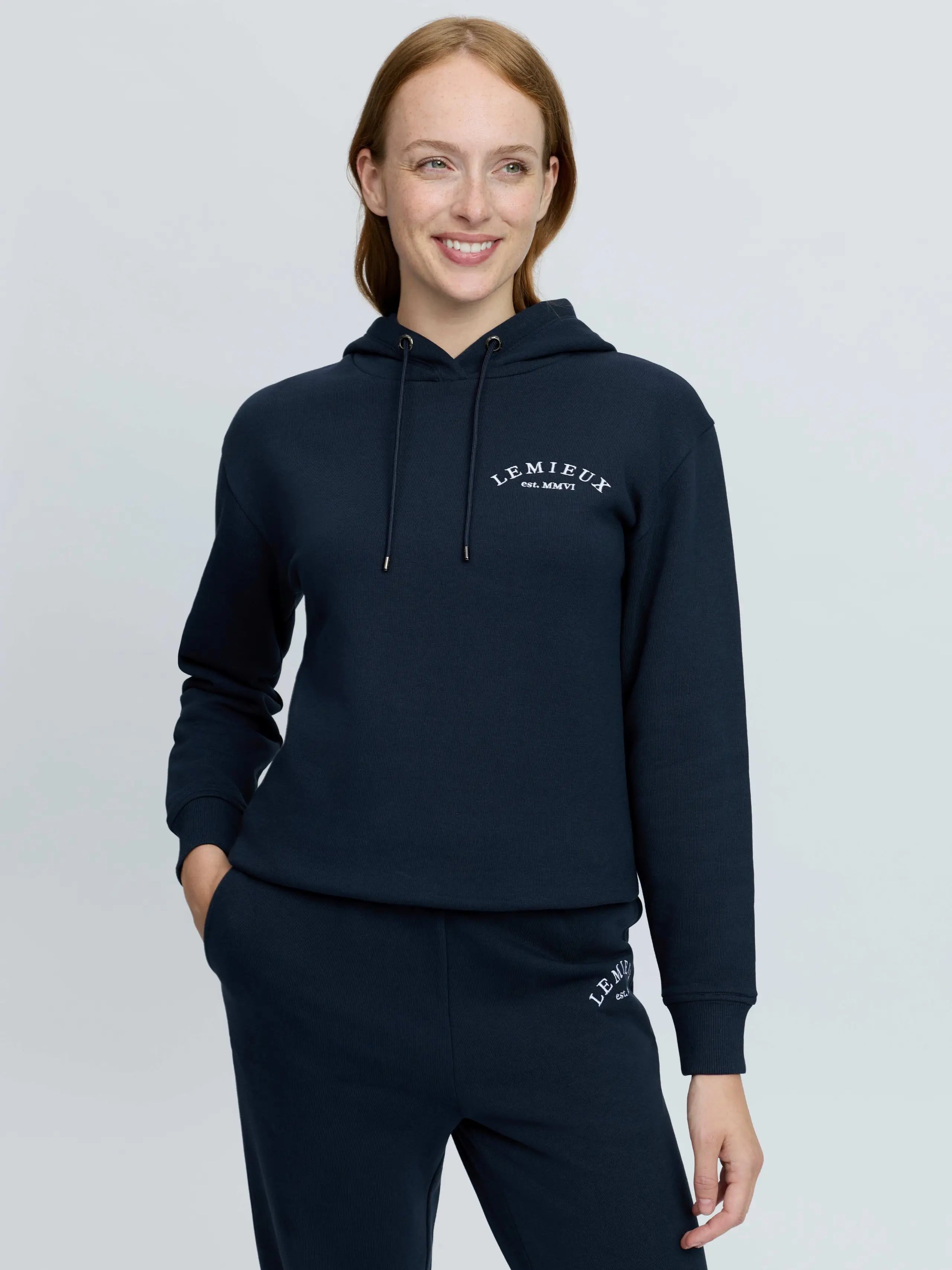 Woman wearing navy blue LeMieux hoodie with embroidered logo and matching joggers.