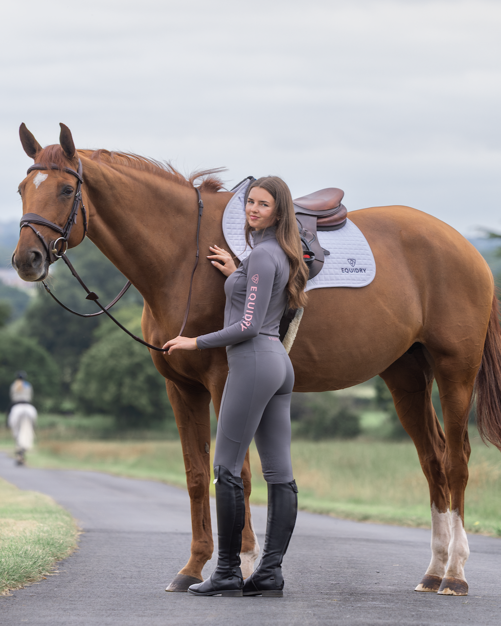 Equestrian style: EQUIDRY grey/pink water repellent riding leggings for women with knee grip. Horse and rider on country road.