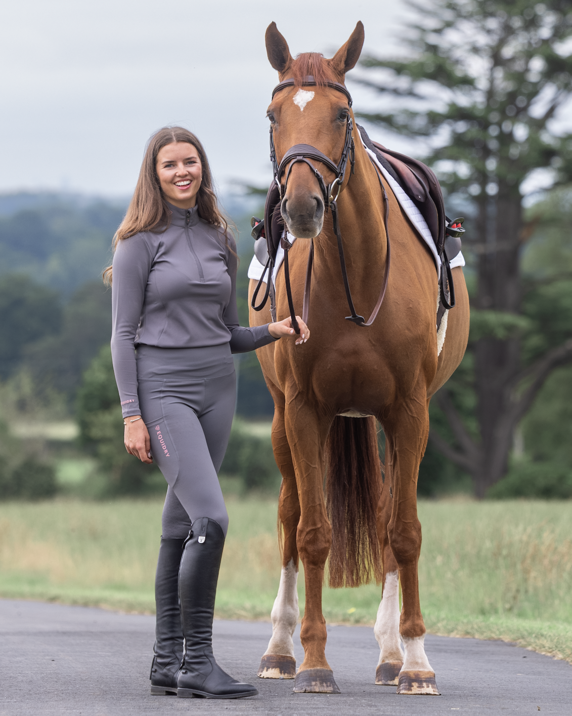 Equestrian: Woman in Grey Equidry Riding Leggings with Pink Logo Standing Next to Chestnut Horse