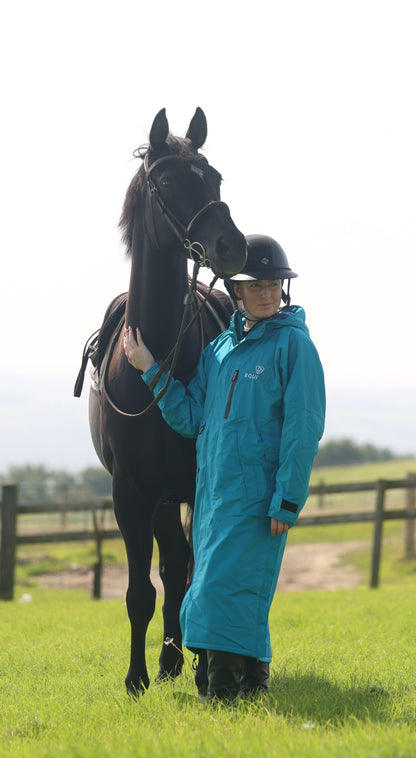 EQUIDRY women's long waterproof horse riding coat in turquoise stood with horse