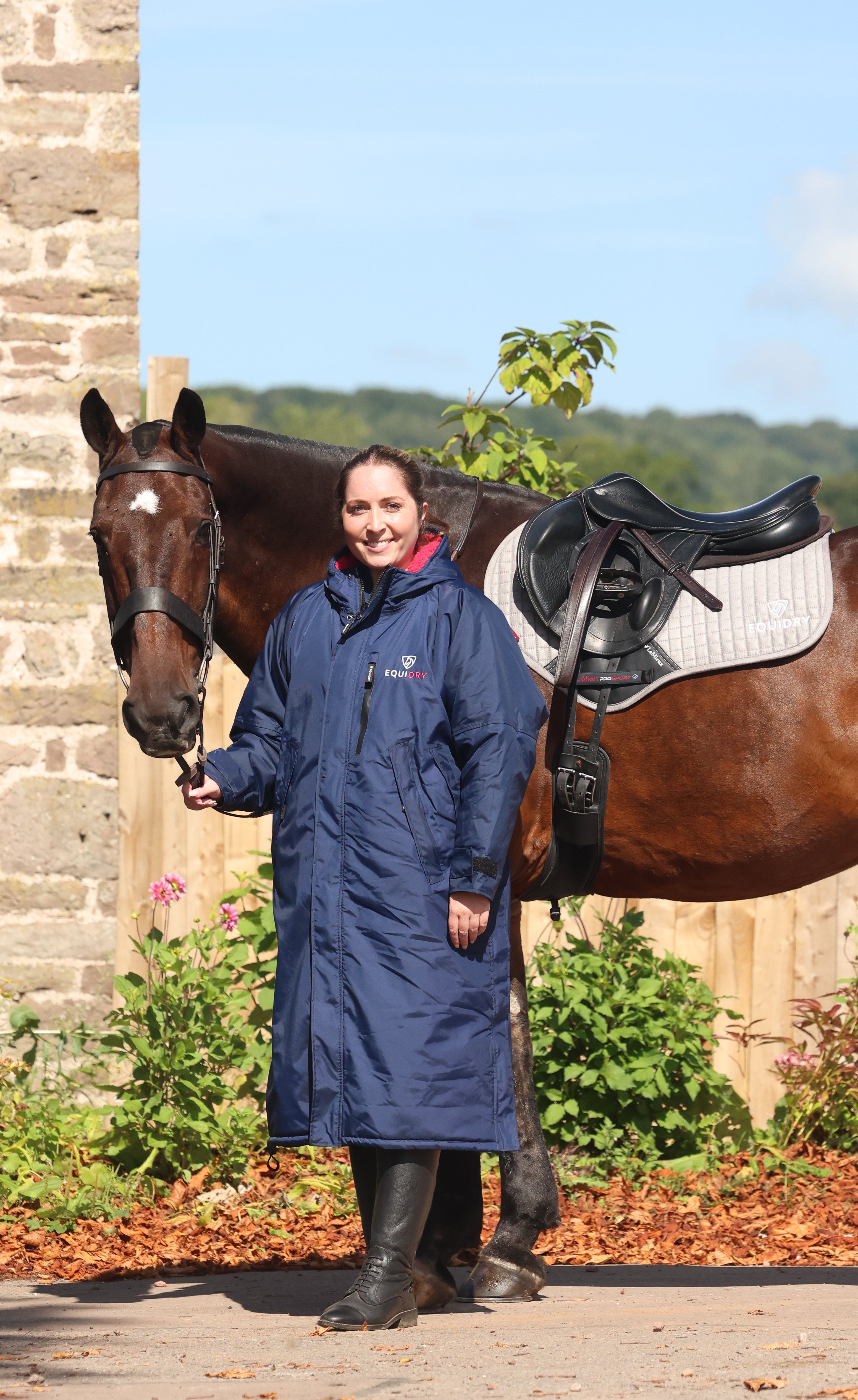EQUIDRY women's long waterproof horse riding coat in navy/raspberry modelled by rider stood with horse