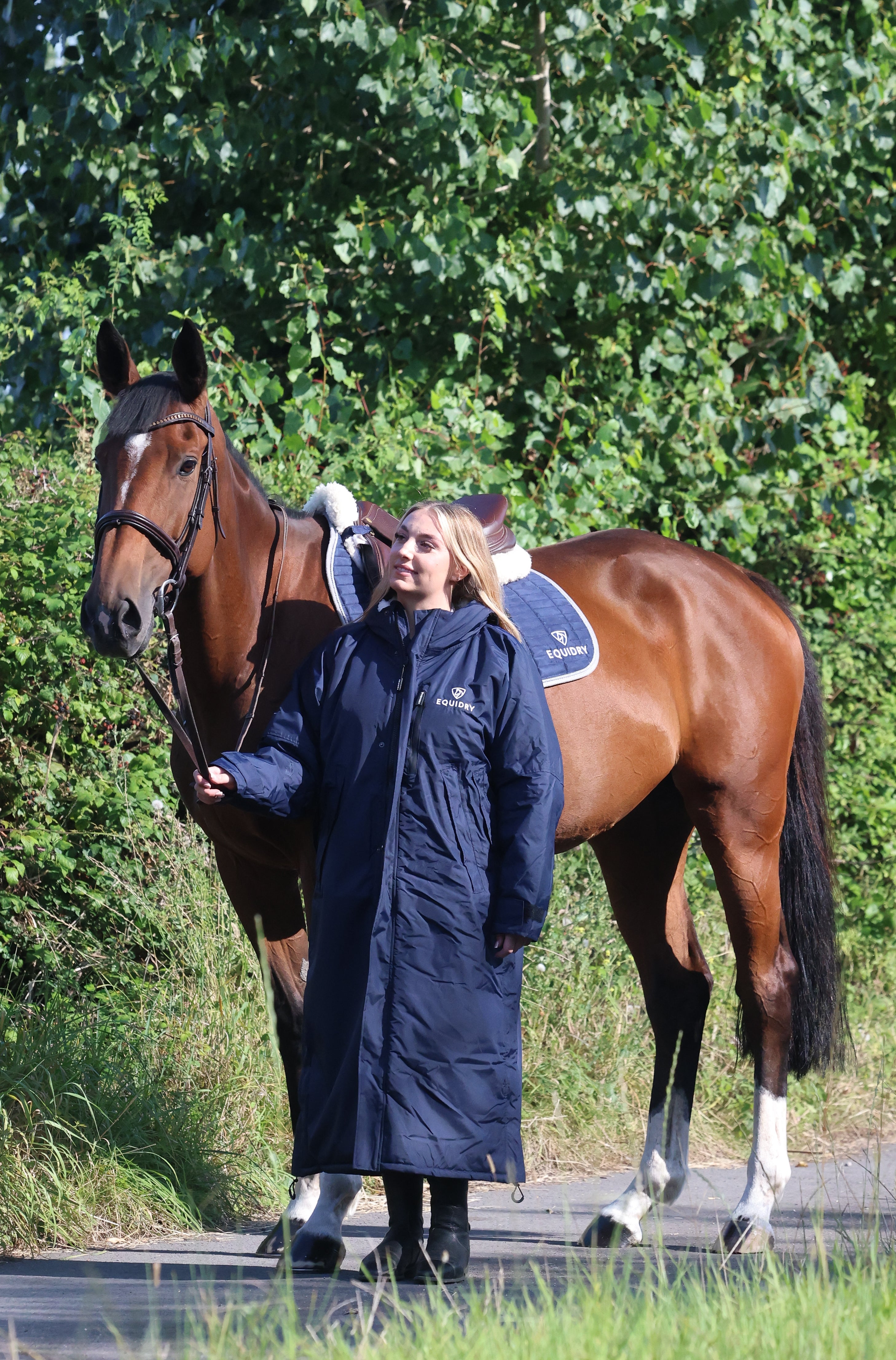 EQUIDRY women's long waterproof horse riding coat in navy/cream worn by rider walking with horse