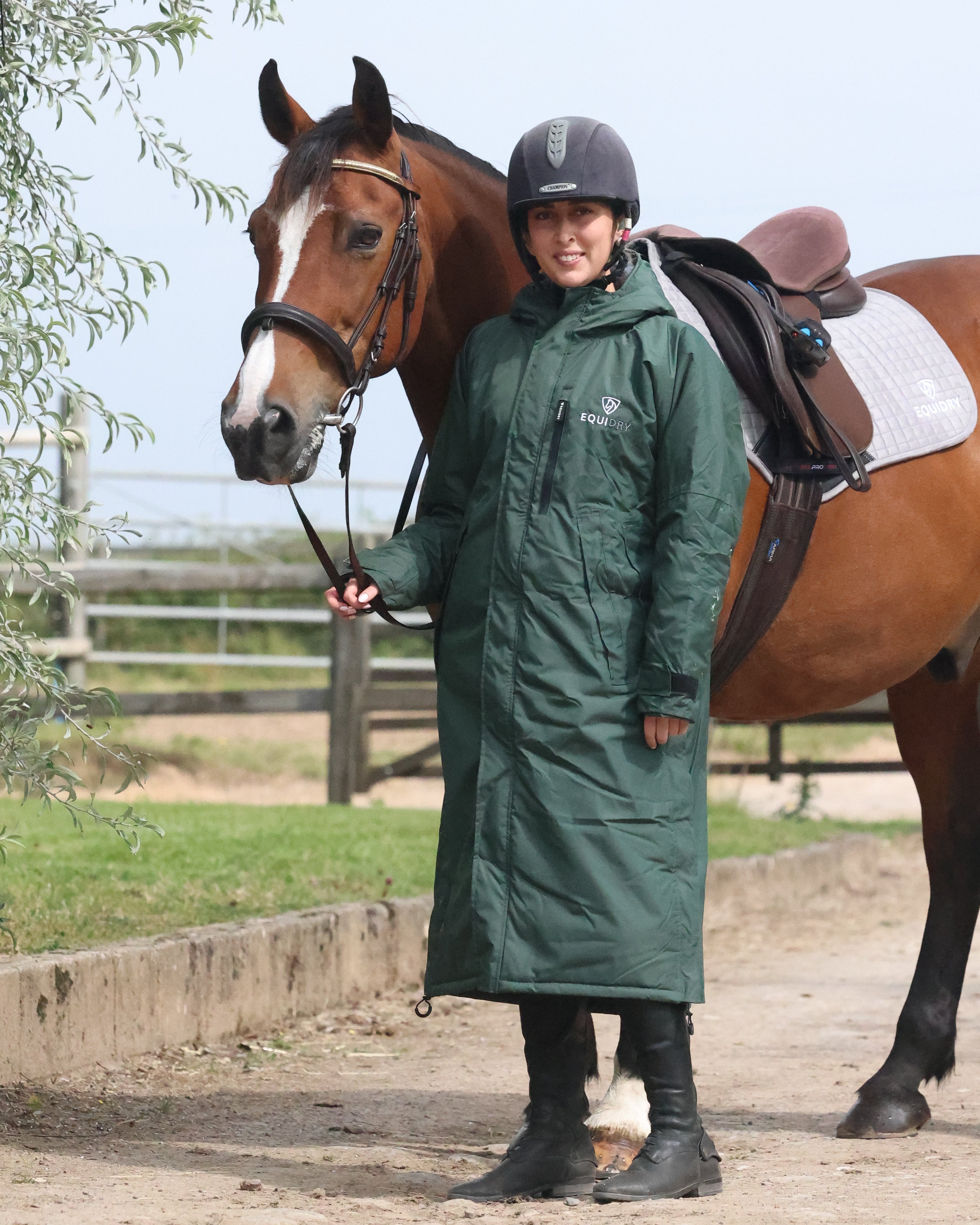 EQUIDRY women's long waterproof horse riding coat in black forest green/green shown by rider stood with horse