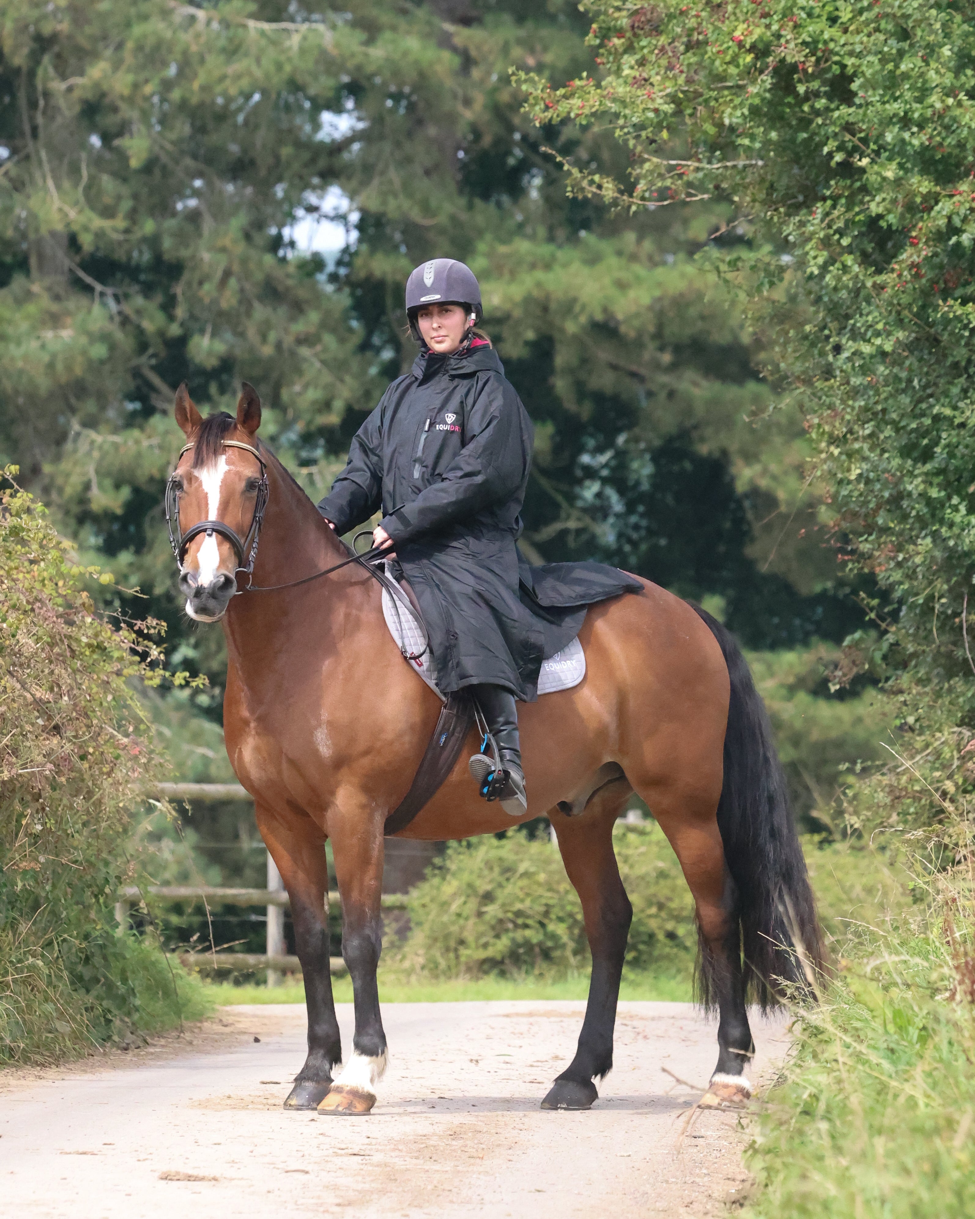 EQUIDRY women's long waterproof horse riding coat in black/peacock pink shown by rider out hacking on horse