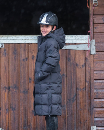 Girl in EQUIDRY Thora Black Waterproof Riding Puffer Coat & Equestrian Helmet at Stable