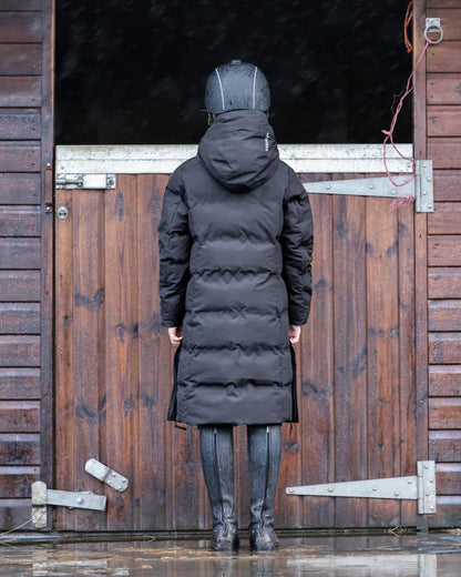 Girl in EQUIDRY Thora Waterproof Black Riding Puffer Coat standing in stable, equestrian apparel, riding gear, winter riding fashion.