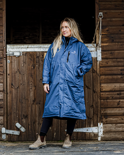 Woman in EQUIDRY Evolution Steel Blue Riding Coat outside stable: Equestrian waterproof fleece lined coat for women.