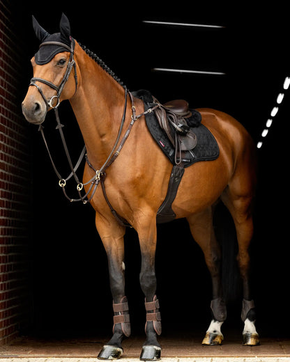 Chestnut horse fully tacked up with LeMieux Crystal Suede Close Contact saddle pad standing in stable.