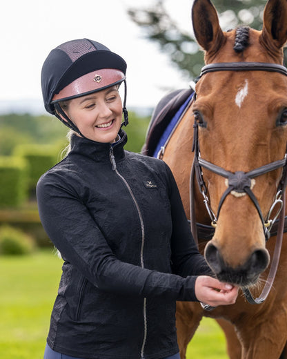 Woman feeding horse wearing Charles Owen Pro II Plus rose gold helmet and black riding jacket. Equestrian lifestyle image.
