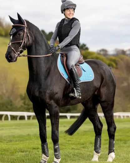 Equestrian: Woman riding black horse with LeMieux Self-Cool Close Contact Square Cool Blue Saddle Pad. Horse riding gear.