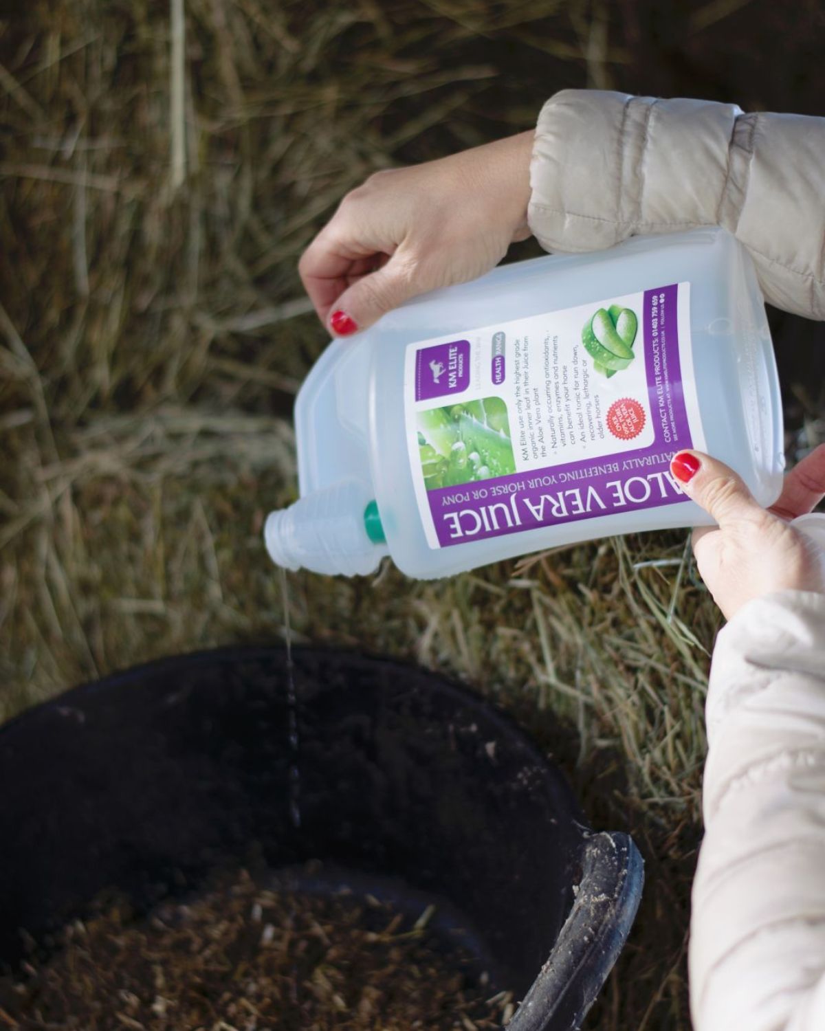 KM Elite Aloe Vera Juice pouring into a horse feed bucket - Natural Equine Supplement for Horse Health and Care